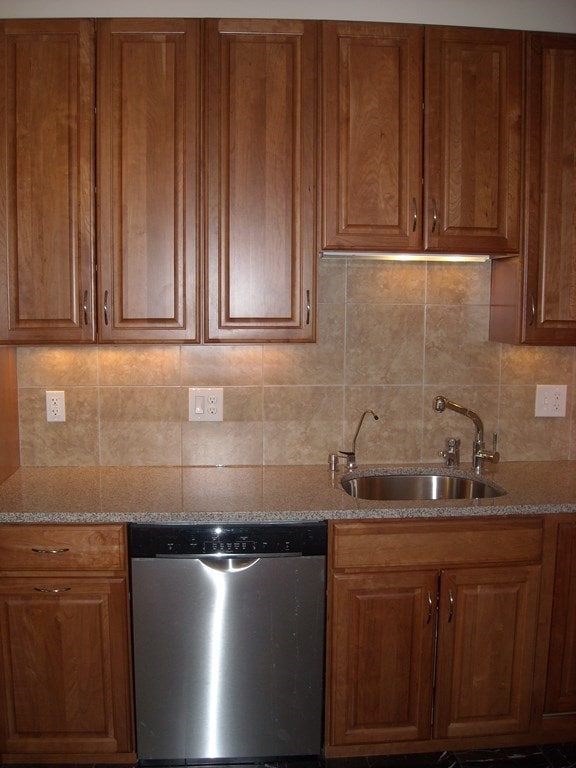 kitchen with dishwasher, light stone countertops, backsplash, and sink