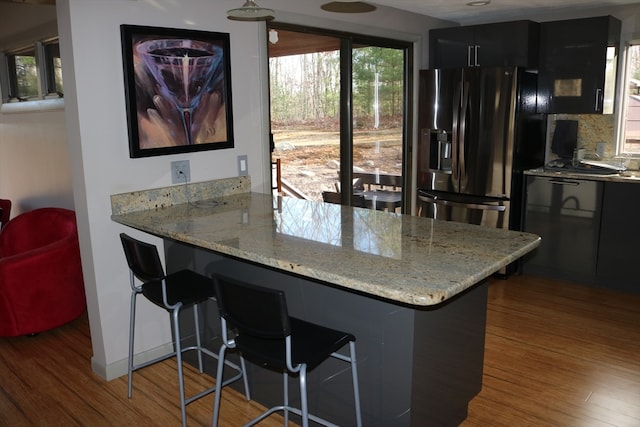 kitchen with wood-type flooring, light stone counters, kitchen peninsula, stainless steel fridge with ice dispenser, and a breakfast bar