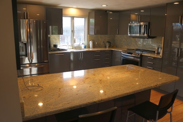 kitchen featuring stainless steel appliances, light hardwood / wood-style floors, tasteful backsplash, light stone countertops, and a kitchen bar