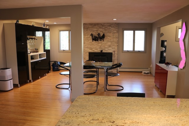 interior space featuring a stone fireplace, light wood-type flooring, and a baseboard heating unit