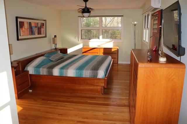 bedroom with a wall unit AC, wood-type flooring, and ceiling fan