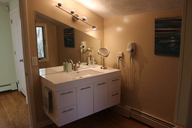 bathroom with hardwood / wood-style floors, vanity, a textured ceiling, and a baseboard heating unit