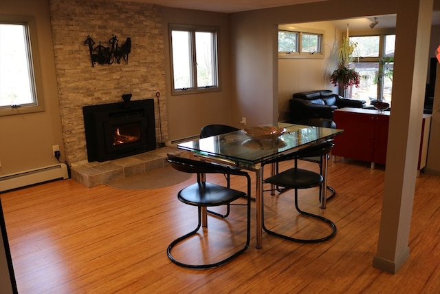 dining room with baseboard heating, a tile fireplace, and light hardwood / wood-style flooring