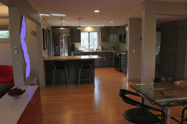 kitchen with range with electric stovetop, stainless steel refrigerator, light hardwood / wood-style floors, a breakfast bar, and kitchen peninsula