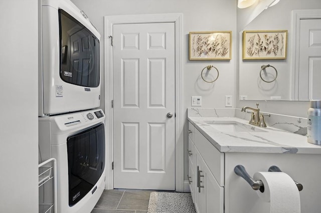 washroom with a sink, dark tile patterned flooring, and stacked washing maching and dryer