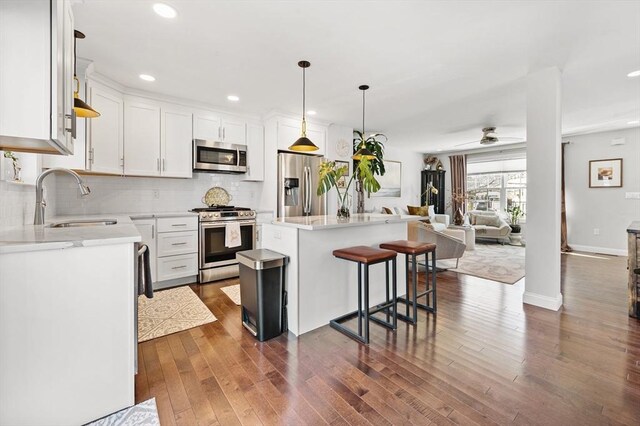 kitchen with a sink, dark wood-type flooring, appliances with stainless steel finishes, open floor plan, and backsplash