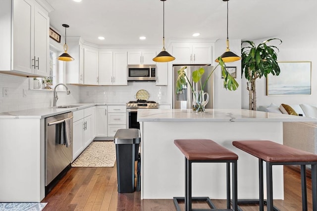 kitchen featuring dark wood finished floors, a kitchen bar, stainless steel appliances, white cabinetry, and a sink