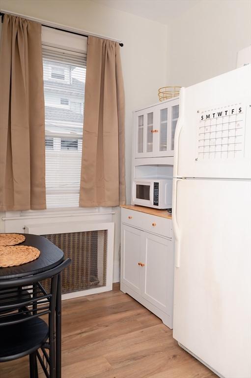 kitchen with white appliances, light hardwood / wood-style floors, white cabinets, and radiator