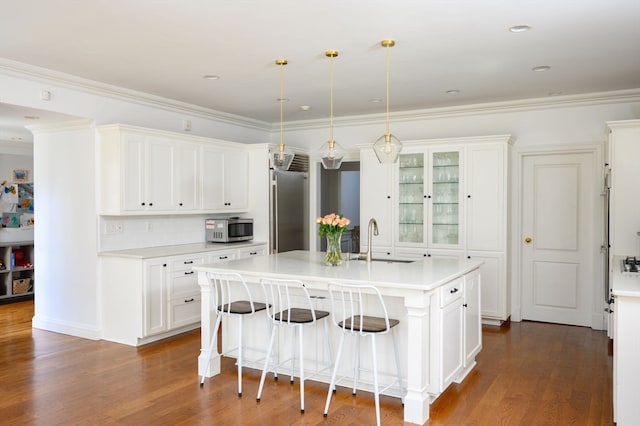 kitchen with sink, an island with sink, stainless steel appliances, pendant lighting, and white cabinets