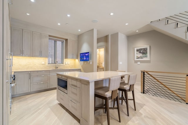 kitchen featuring light hardwood / wood-style flooring, a breakfast bar, sink, backsplash, and a center island