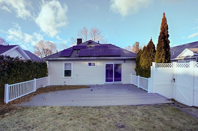 back of house with solar panels, a lawn, and a wooden deck