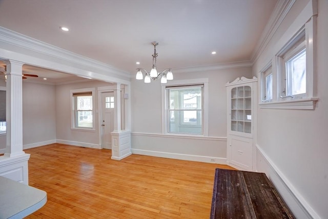 unfurnished dining area with ceiling fan with notable chandelier, crown molding, a wealth of natural light, and light hardwood / wood-style flooring