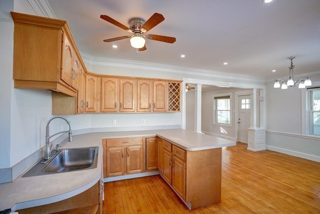 kitchen featuring pendant lighting, sink, ornamental molding, kitchen peninsula, and decorative columns