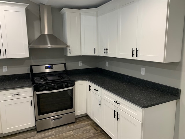 kitchen with stainless steel gas range oven, wall chimney range hood, white cabinetry, and dark hardwood / wood-style floors