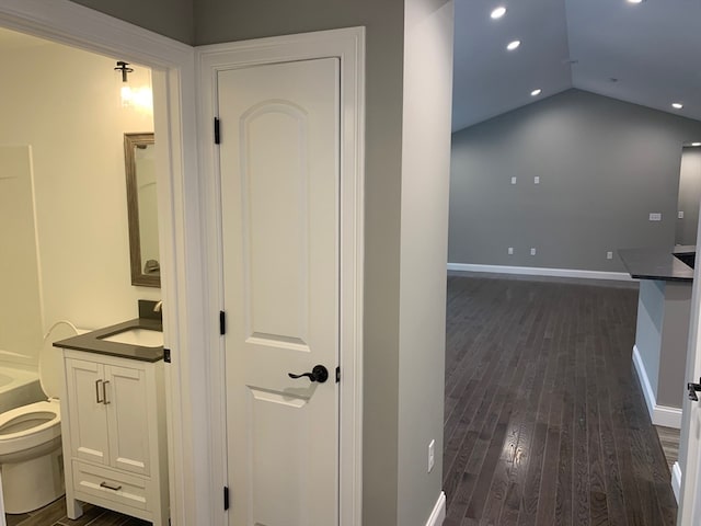 corridor with lofted ceiling, dark hardwood / wood-style floors, and sink