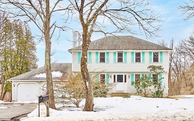 colonial house featuring a garage, driveway, a shingled roof, and a chimney