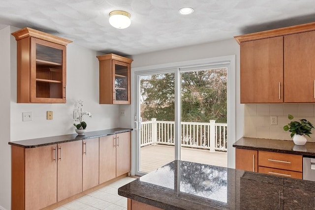 kitchen featuring light tile patterned floors, glass insert cabinets, dark stone counters, and backsplash