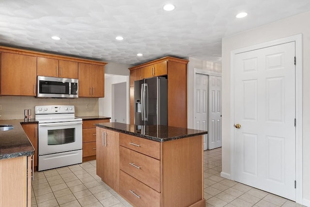 kitchen featuring light tile patterned floors, appliances with stainless steel finishes, backsplash, a center island, and dark stone counters