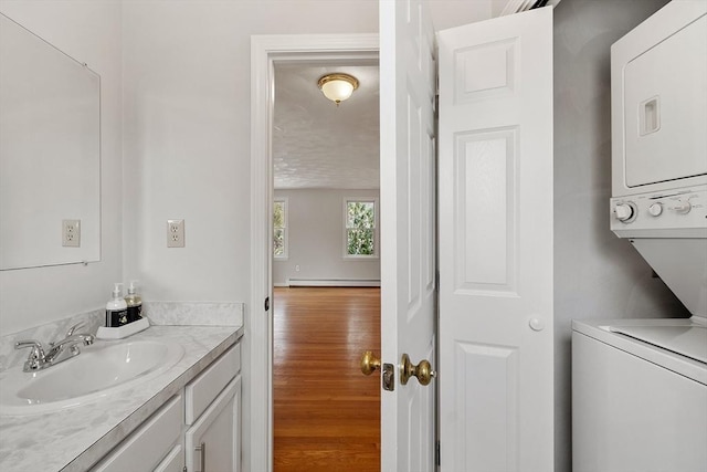 washroom with a baseboard radiator, stacked washer / dryer, a sink, wood finished floors, and laundry area