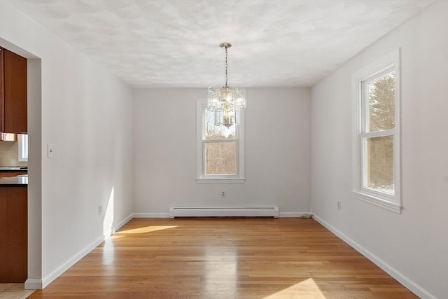 unfurnished dining area featuring a baseboard heating unit, light wood-type flooring, a chandelier, and baseboards