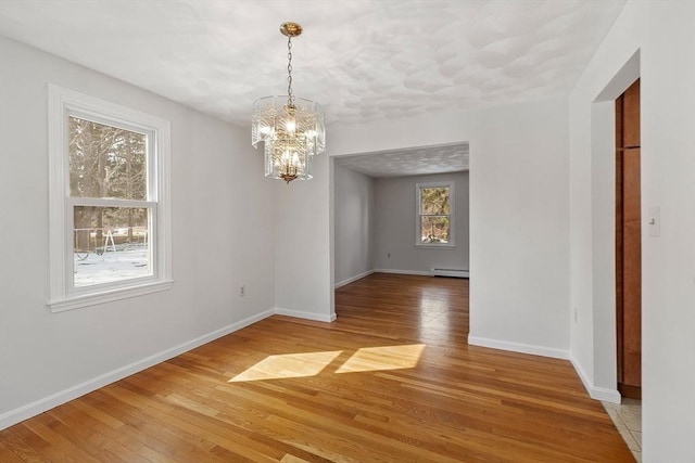 unfurnished dining area featuring a chandelier, a baseboard radiator, light wood-style flooring, and baseboards