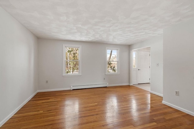 empty room featuring a baseboard heating unit, a textured ceiling, wood finished floors, and baseboards