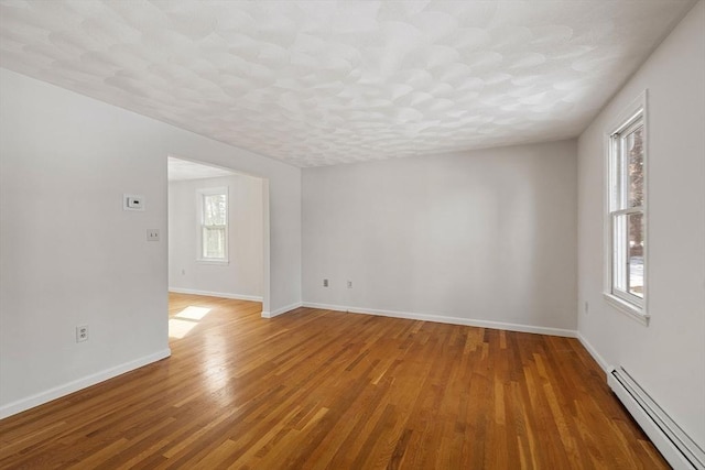 empty room with a baseboard radiator, a textured ceiling, baseboards, and wood finished floors