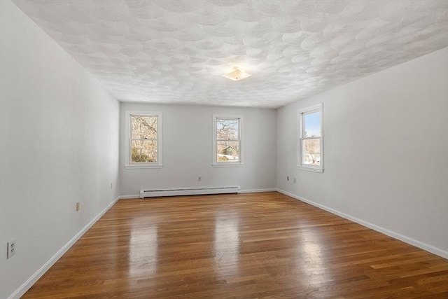 spare room with a textured ceiling, baseboards, baseboard heating, and wood finished floors