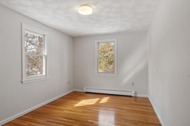 spare room featuring a baseboard heating unit, wood finished floors, and baseboards