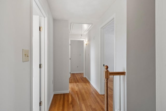 hallway featuring attic access, baseboards, and light wood finished floors