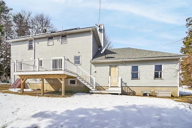 snow covered house featuring a shingled roof, a chimney, and a wooden deck