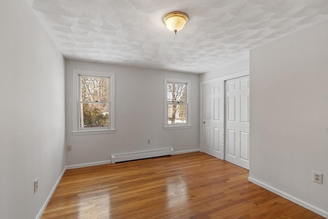 unfurnished bedroom featuring a baseboard radiator, a closet, baseboards, and wood finished floors