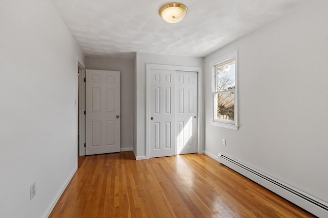 unfurnished bedroom with light wood finished floors, baseboards, a baseboard heating unit, and a closet