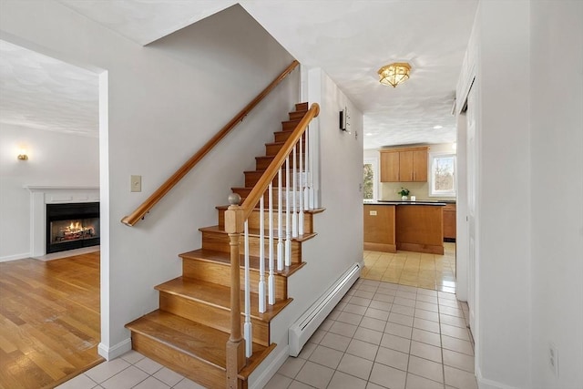 stairs with tile patterned flooring, a baseboard heating unit, baseboards, and a fireplace with flush hearth