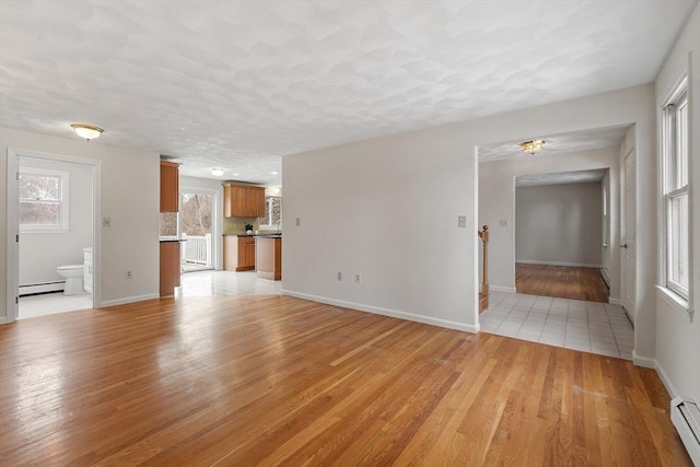 unfurnished living room featuring a textured ceiling, a baseboard heating unit, baseboards, light wood-style floors, and baseboard heating