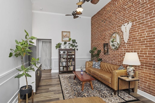 living room featuring a wainscoted wall, crown molding, dark wood finished floors, ceiling fan, and brick wall