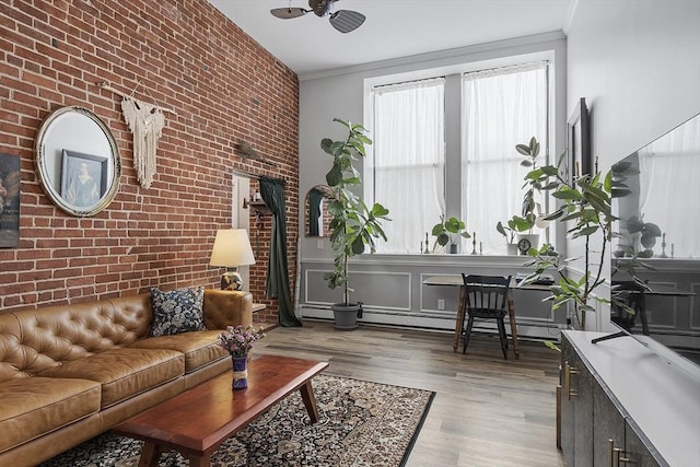 living area with crown molding, light wood finished floors, baseboard heating, an accent wall, and brick wall