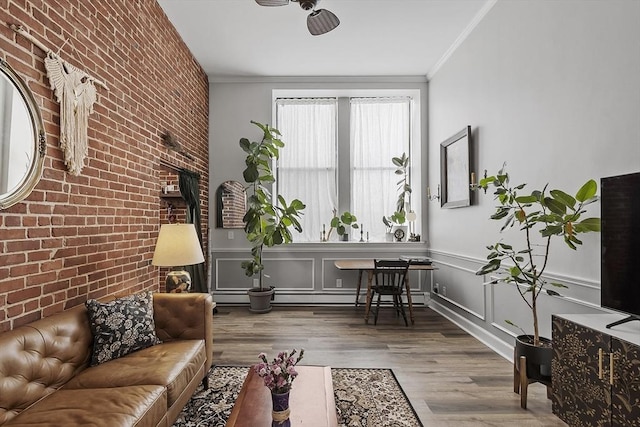 living area featuring wainscoting, brick wall, an accent wall, ornamental molding, and wood finished floors