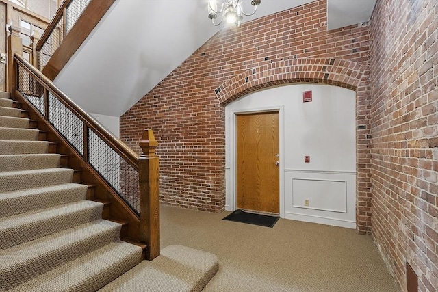 carpeted entryway with vaulted ceiling, brick wall, and stairs