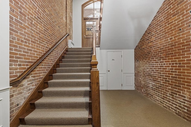 stairs with lofted ceiling, brick wall, and carpet