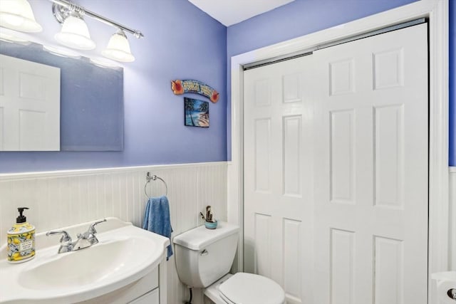 bathroom featuring vanity, toilet, and a wainscoted wall