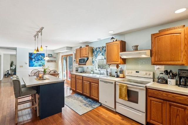 kitchen with a sink, white appliances, light countertops, a kitchen bar, and under cabinet range hood