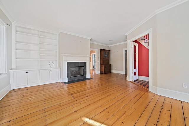 unfurnished living room with built in features, a tile fireplace, hardwood / wood-style flooring, and crown molding