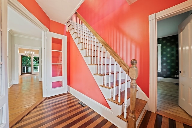 stairway with hardwood / wood-style floors, a chandelier, and ornamental molding