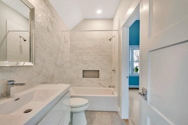 full bathroom with toilet, tiled shower / bath, wood-type flooring, vaulted ceiling, and vanity