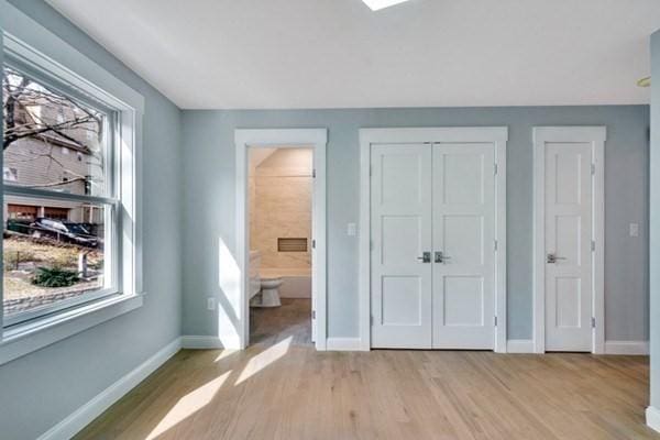 unfurnished bedroom with multiple windows, ensuite bathroom, multiple closets, and light hardwood / wood-style floors