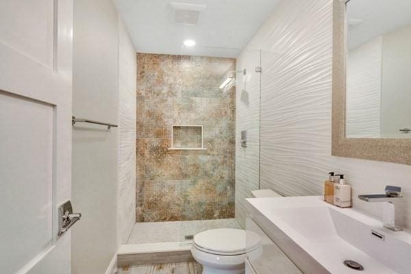 bathroom featuring tiled shower, vanity, toilet, and tile walls