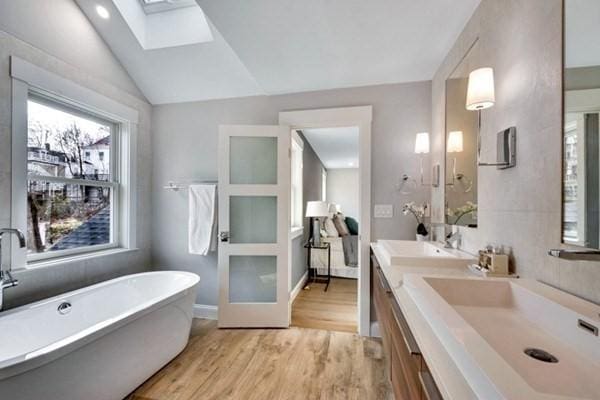 bathroom with hardwood / wood-style flooring, vanity, vaulted ceiling with skylight, and a bathtub