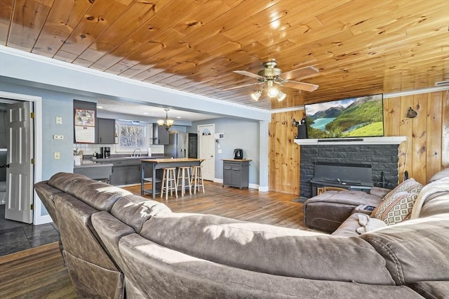 living room with wood ceiling, ceiling fan with notable chandelier, wooden walls, sink, and dark hardwood / wood-style floors