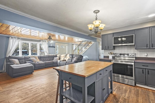 kitchen featuring wooden counters, tasteful backsplash, ceiling fan with notable chandelier, stainless steel appliances, and dark wood-type flooring